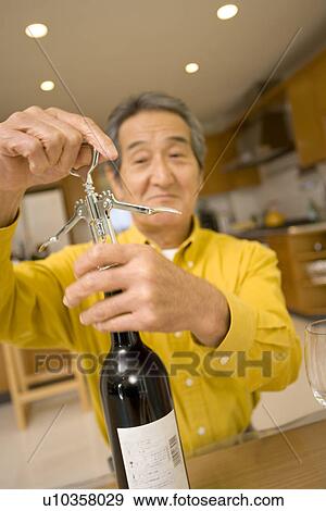 Stock Photo - A Senior Adult Man Opening a Bottle of Wine, Front View, Differential Focus. Fotosearch