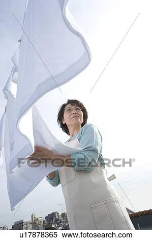 Stock Photography - A Senior Adult Woman Hanging Out the Laundry Under the Sky, Side View, Low Angle View. Fotosearch