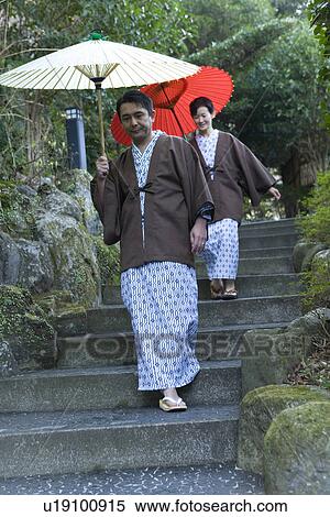 Stock Photography - Mature Adult Couple in Yukata Going Down Stairs with Paper Umbrellas, Front View, Full Length, Low Angle View. Fotosearch