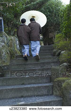 Stock Image - Mature Adult Couple in Yukata Going Up Stairs with a Paper Umbrella, Rear View, Full Length, Low Angle View. Fotosearch