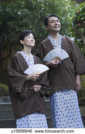 Stock Photograph - Mature Adult Couple in Yukata Holding Fans, Front View, Three Quarter Length, Low Angle View. Fotosearch