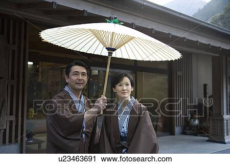 Stock Image - Mature Adult Couple in Yukata Sharing a Paper Umbrella, Waist Up, Front View. Fotosearch