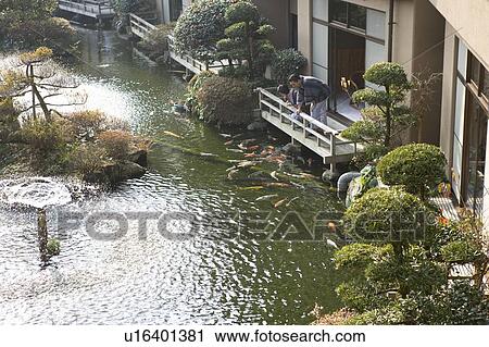 Stock Image - Mature Adult Couple Looking at Carp From the Balcony, Side View, Full Length, High Angle View. Fotosearch