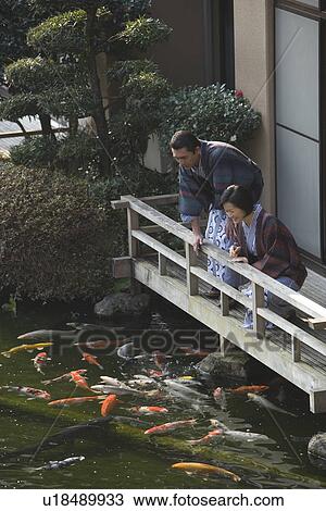 Stock Image - Mature Adult Couple Looking at Carp From the Balcony, Side View, Full Length, High Angle View. Fotosearch