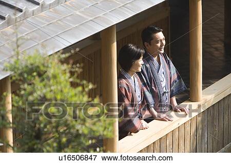 Stock Photo - Mature Adult Couple Standing at a Hallway and Looking Outside, Side View, High Angle View, Waist Up. Fotosearch