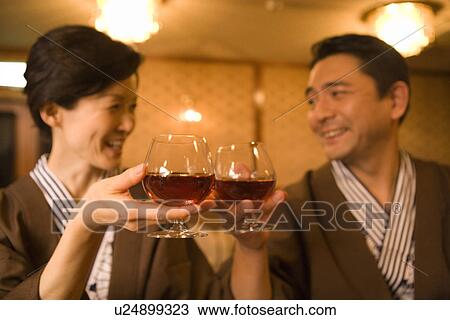 Stock Image - Mature Adult Couple Toasting With Brandy, Front View, Head and Shoulder, Differential Focus. Fotosearch
