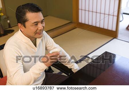 Stock Photo - Mature Adult Man Drinking Tea in the Room of a Japanese-style Hotel, High Angle View, Side View, Waist Up. Fotosearch