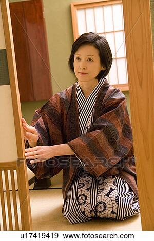 Stock Photo - Mature Adult Woman Sitting and Opening the Sliding Door, Front View, Three Quarter Length. Fotosearch