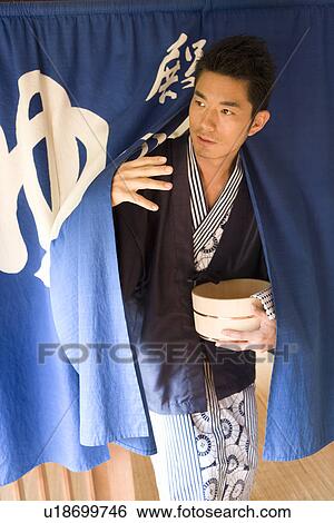 Stock Photograph - A Mid Adult Man in Yukata Going Through a Short Split Curtain, Front View. Fotosearch