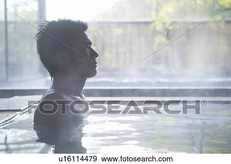 Stock Photo - A Mid Adult Man Sitting in the Outdoor Hot Spring Bath, Side View. Fotosearch