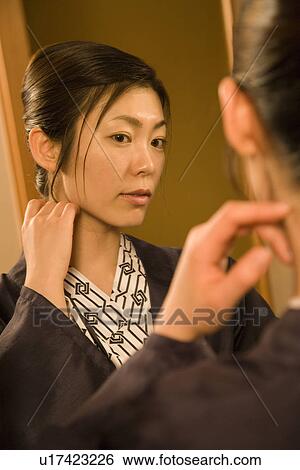 Stock Photograph - A Mid Adult Woman in Yukata, Looking Herself in a Mirror, Side View, Close Up. Fotosearch