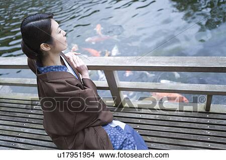 Picture - A Mid Adult Woman in Yukata, Sitting at the Wooden Balcony, High Angle View, Side View. Fotosearch