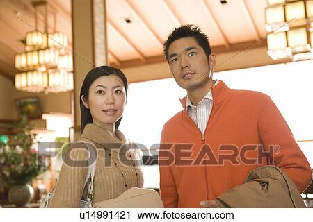 Stock Image - Mid Adult Couple Arriving at a Japanese Traditional Inn, Waist Up, Low Angle View, Differential Focus. Fotosearch