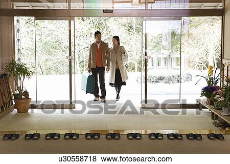 Stock Photo - Mid Adult Couple Arriving at a Japanese Traditional Inn, Front View, Full Length. Fotosearch