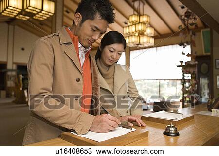 Stock Image - Mid Adult Couple at the Checking-in Counter in a Traditional Japanese Inn, Low Angle View, Waist Up. Fotosearch