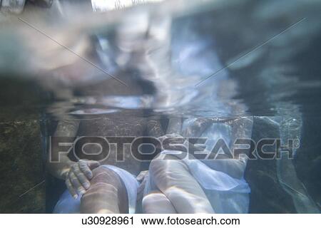 Stock Image - Mid Adult Couple Sitting in the Outdoor Hot Spring Bath, Shooting in the Water, Front View. Fotosearch
