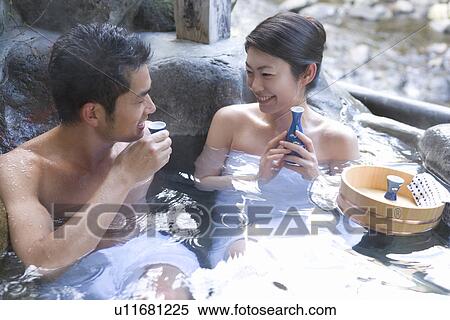 Stock Photography - Mid Adult Couple Sitting in the Outdoor Hot Spring Bath, Drinking Sake, Front View, Side View. Fotosearch