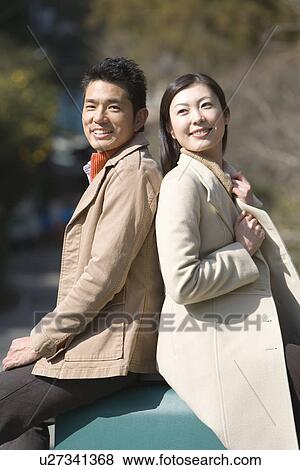 Stock Photo - Smiling Mid Adult Couple Sitting Back to Back, Side View, Differential Focus. Fotosearch