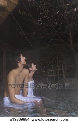 Picture - Man and woman in a hot tub looking up the sky, side view, Japan. Fotosearch