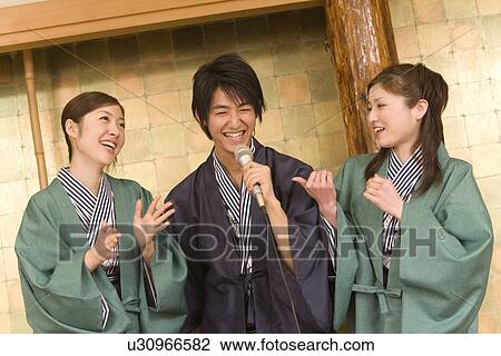 Stock Image - Man standing between two women and singing, front view, Japan. Fotosearch