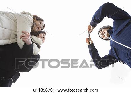 Stock Image - Man taking a picture of two women, low angle view, white background, Japan. Fotosearch