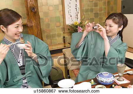 Stock Photo - Two women having dinner, one taking a picture, front view, Japan. Fotosearch