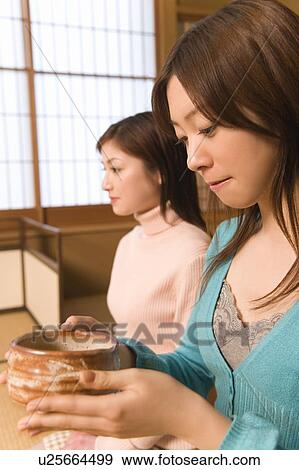 Stock Photo - Two women in a tea room, one holding a tea cup, side view, Japan. Fotosearch