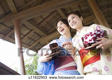 Stock Image - Two women in Yukata holding wooden pails, low angle view, Japan. Fotosearch