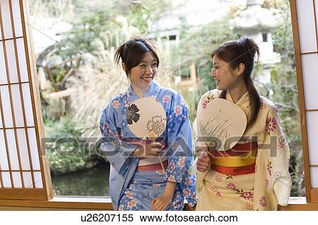 Stock Photography - Two women in Yukata sitting and holding Japanese fans, front view, Japan. Fotosearch