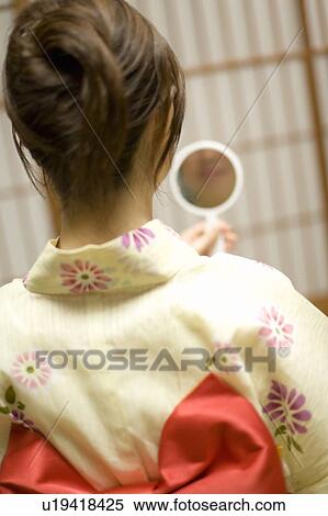 Stock Photography - Woman in Yukata holding a hand mirror, rear view, Japan. Fotosearch