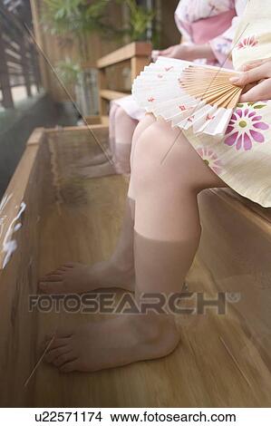 Picture - Women in Yukata soaking legs in the footbath, one holding a Japanese folding fan, side view, close up, Japan. Fotosearch
