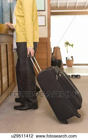 Stock Image - Young couple standing at the hotel reception, man holding a suitcase, side view, Japan. Fotosearch