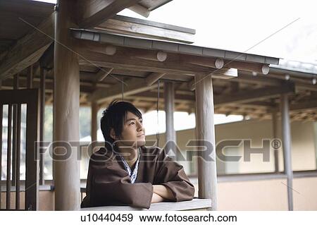 Stock Photo - Young man in Yukata leaning on a wooden railing at a Japanese inn, side view, Japan. Fotosearch
