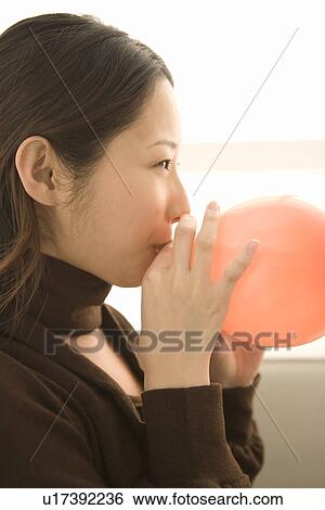 Stock Photograph - A woman blowing a pink balloon, side view. Fotosearch