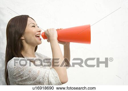 Stock Image - A woman holding a megaphone, side view, white background. Fotosearch