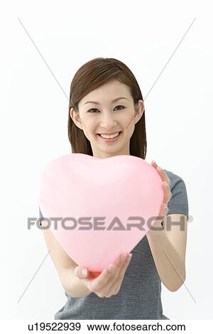 A woman holding up a pink heart, looking at camera, front view, white background View Large Photo Image Stock Photo - A woman holding up a pink heart, looking at camera, front view, white background. Fotosearch