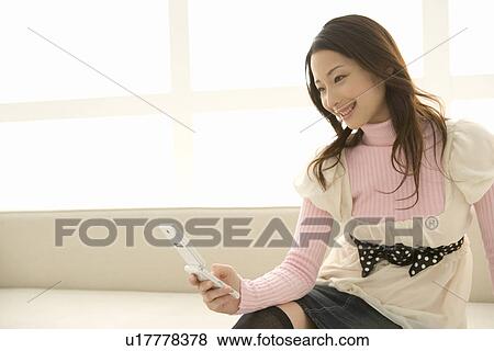 Stock Photo - A woman sitting and using a mobile phone, side view. Fotosearch