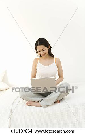 A woman sitting on a bed and using a laptop, front view, white background View Large Photo Image Picture - A woman sitting on a bed and using a laptop, front view, white background. Fotosearch