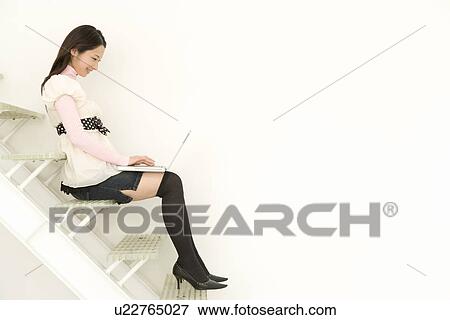 A woman sitting on stairs and using a laptop, side view, white background, copy space View Large Photo Image Stock Photo - A woman sitting on stairs and using a laptop, side view, white background, copy space. Fotosearch