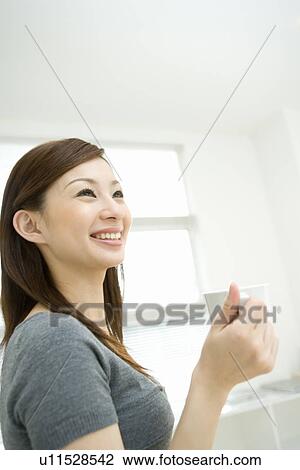 Stock Image - A woman smiling and holding a cup, side view. Fotosearch