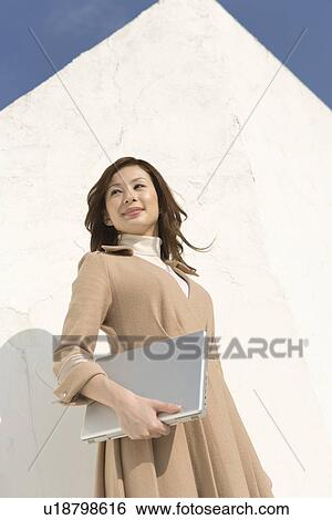 A woman smiling and holding a laptop, low angle view View Large Photo Image Stock Photograph - A woman smiling and holding a laptop, low angle view. Fotosearch