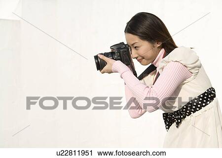 Stock Image - A woman taking a photograph, side view, white background. Fotosearch