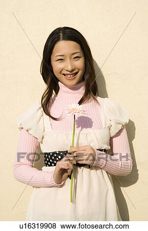 Stock Photo - Portrait of a woman holding single flower, looking at camera, front view, pink background. Fotosearch