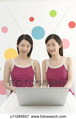 Stock Photo - Portrait of Two Young Twin Sisters Using a Laptop, Front View . Fotosearch