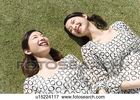 Twin sisters lying down on lawn, smiling, high angle view View Large Photo Image Stock Photo - Twin sisters lying down on lawn, smiling, high angle view. Fotosearch
