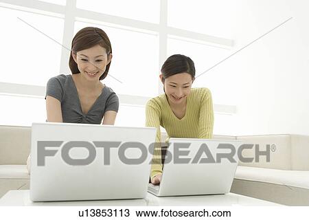 Two women sitting on a couch and using laptops, front view, low angle view View Large Photo Image Stock Image - Two women sitting on a couch and using laptops, front view, low angle view. Fotosearch