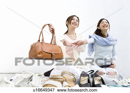 Stock Photo - Two women smiling and trying to sell a bag at a flea market, one holding a bag, front view, white background, low angle view. Fotosearch