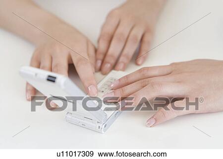 Stock Photo - Two Women's Hands Using a Mobile Phone, High Angle View. Fotosearch