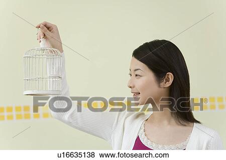 Stock Photo - Woman holding a birdcage, side view. Fotosearch