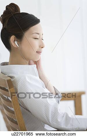Stock Photography - Woman sitting and listening to music, closing eyes, side view. Fotosearch